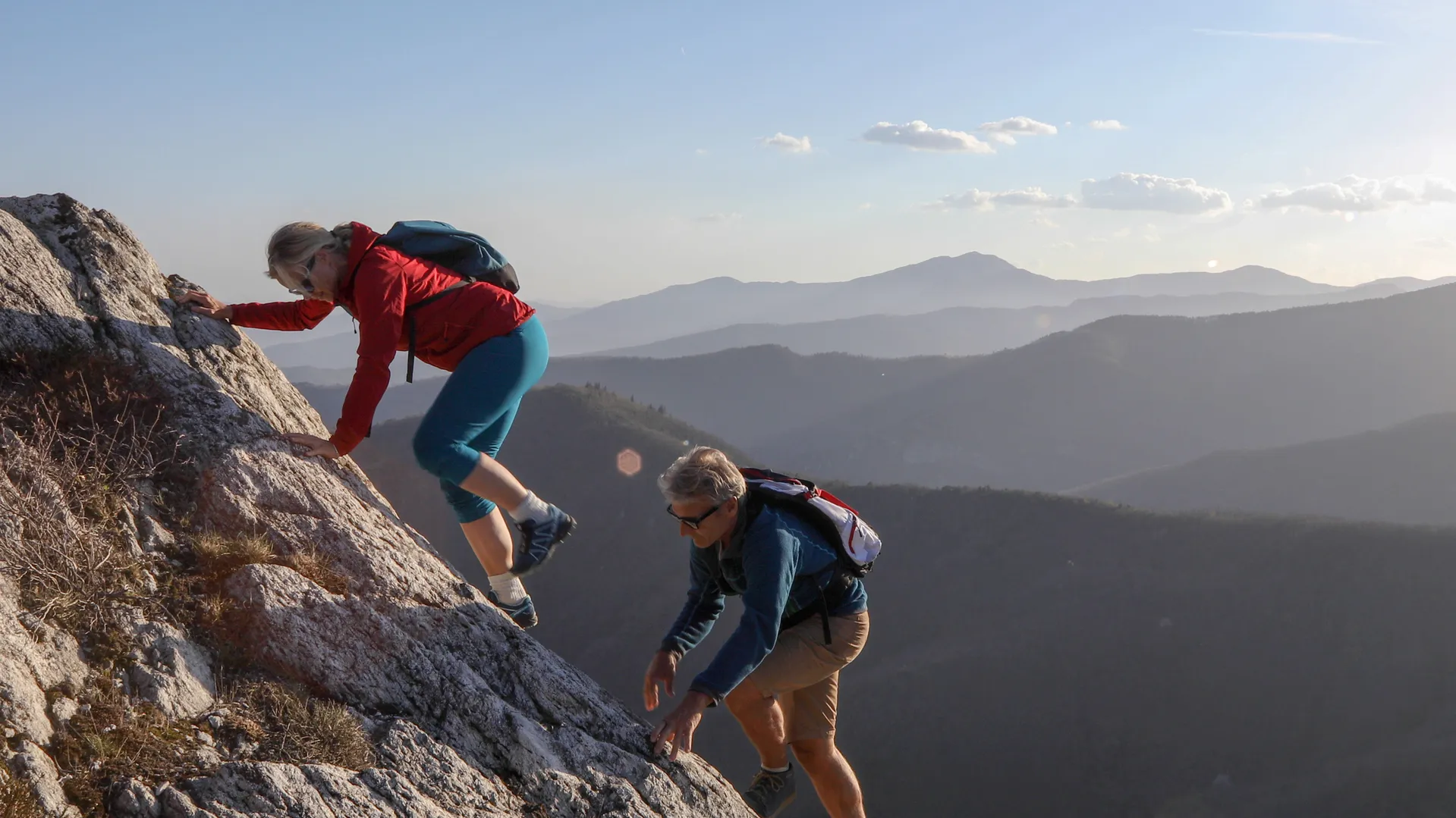 middle age couple scrambling up ridge line with sunset in the background