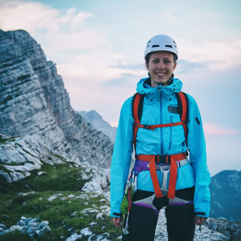 female mountain guide wearing a blue jumper, climbing harness and helmet
